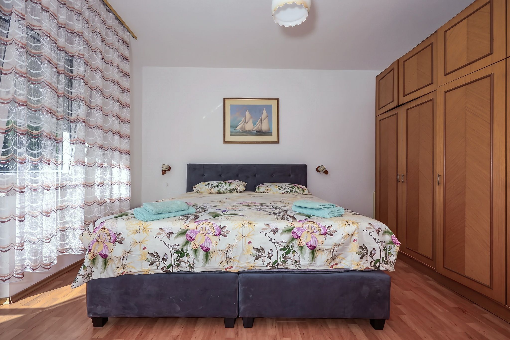 The main bedroom, with floral bedding and a framed painting of sailing boats