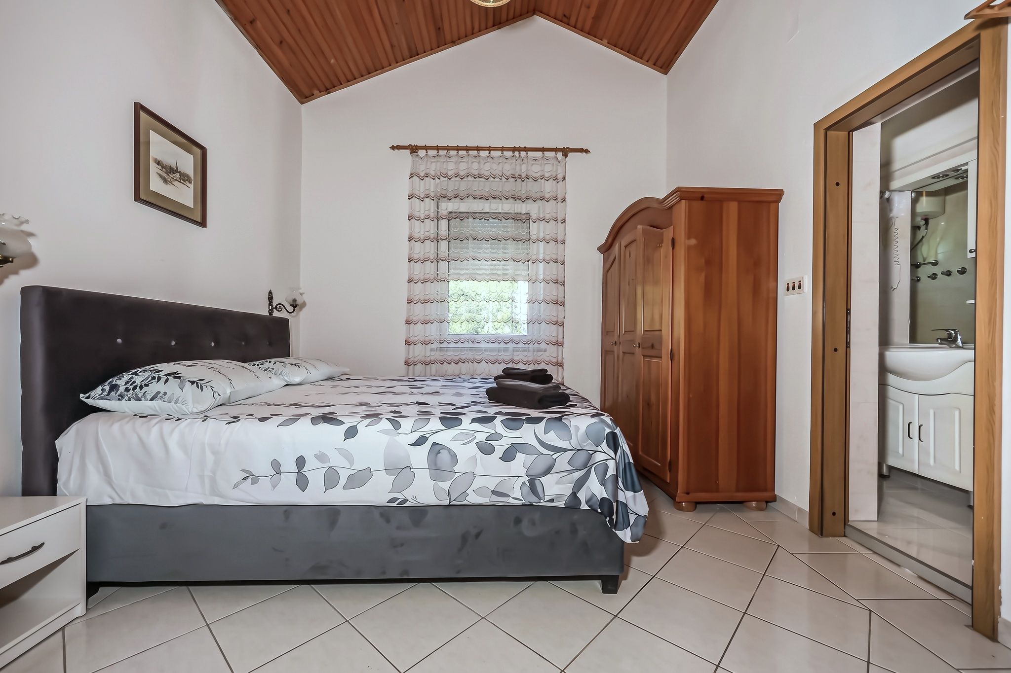 The main bedroom, with a grey upholstered bed and the en-suite beyond