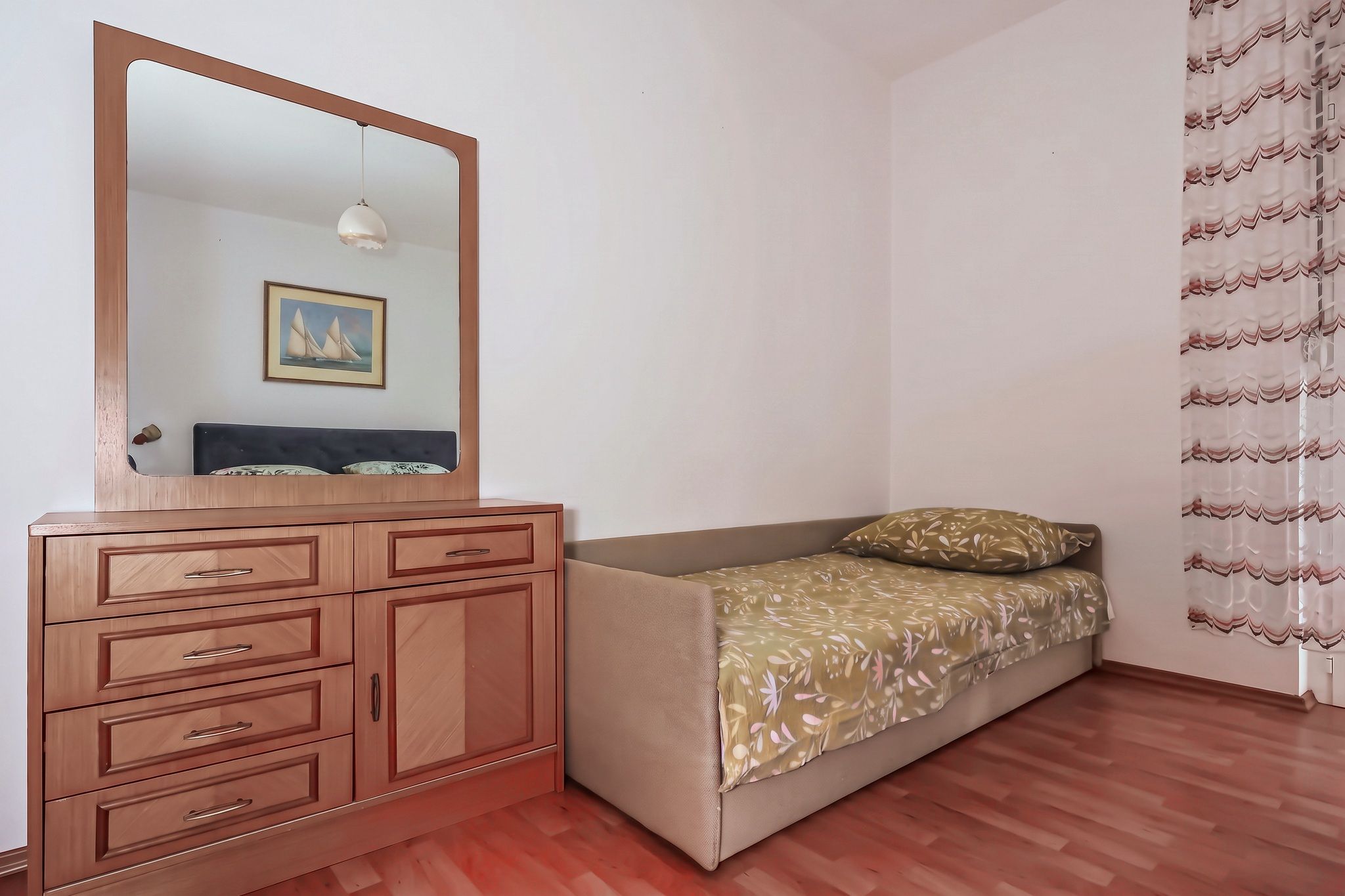 The third bed in the main bedroom, beside a chest of drawers and a mirror