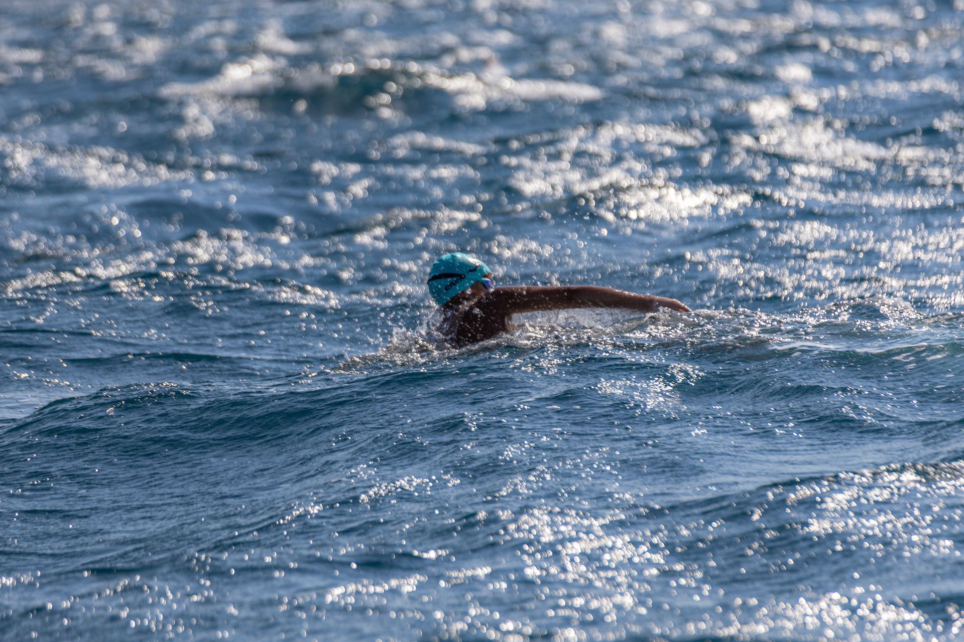 A swimmer in a turquoise cap mid-stroke in open, glittering sea