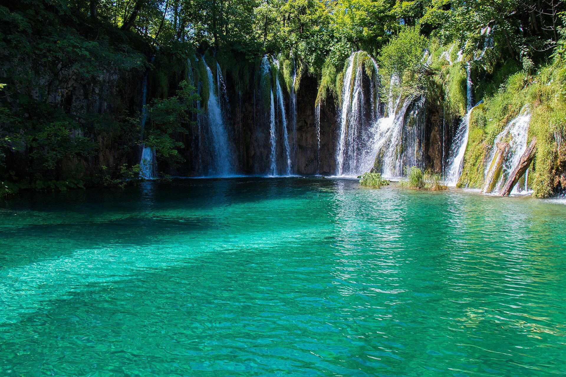 Waterfalls dropping through green forest into a clear turquoise lake